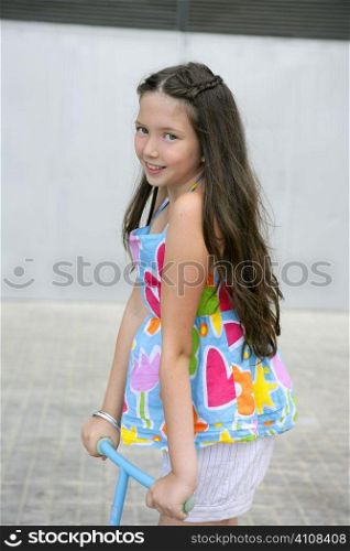 Brunette little girl with scooter in gray city background