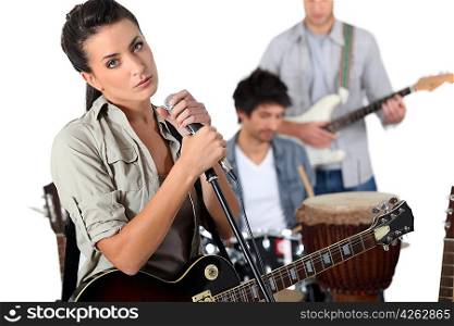 brunette singer with guitar and microphone and male musicians in background