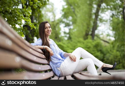 Brunette sitting on a bench in a summer park