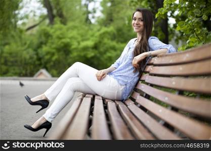 Brunette sitting on a bench in a summer park