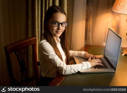 Brunette smiling schoolgirl posing in cabinet with laptop