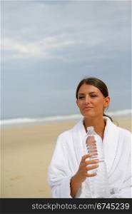 Brunette stood on a beach holding bottle of water