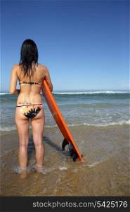Brunette stood on beach with surf board