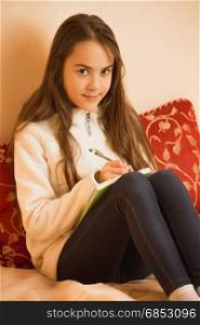 Brunette teen girl writing in diary at bedroom