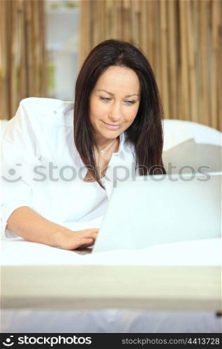 Brunette typing on laptop in bed