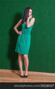 brunette weared green dress standing indoors, against green wall