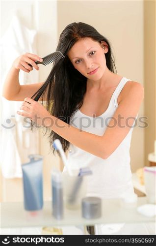 Brunette woman brushing long hair in front of bathroom mirror