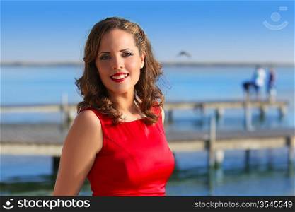 Brunette woman dress in red smiling relaxed on a blue lake jetty