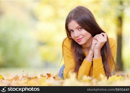 Brunette woman laying in autumn park. Portrait of a beautiful young brunette woman laying in the autumn park