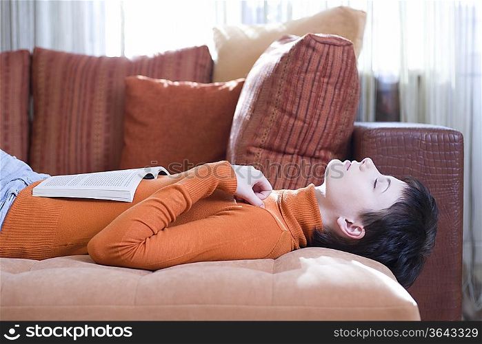 Brunette woman lies on her back with eyes closed and an open book