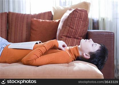 Brunette woman lies on her back with eyes closed and an open book