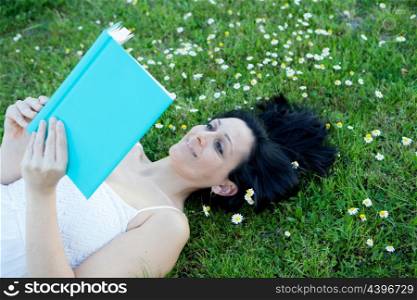 Brunette woman lying on a flowered meadow reading a book
