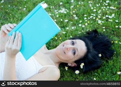 Brunette woman lying on a flowered meadow reading a book