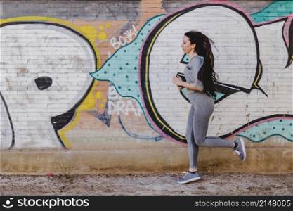 brunette woman running against concrete wall
