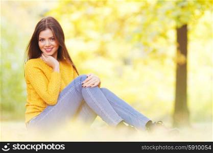 Brunette woman sitting in autumn park. Portrait of a beautiful young brunette woman sitting in the autumn park