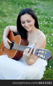 Brunette woman sitting on a flowered meadow playing guitar