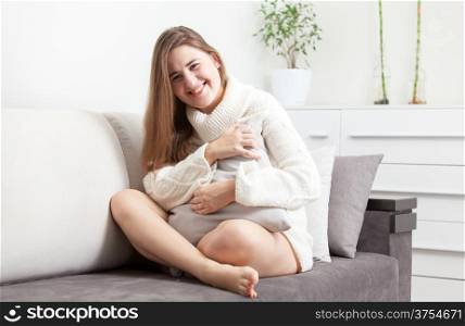 Brunette woman sitting on sofa with crossed legs and hugging pillow