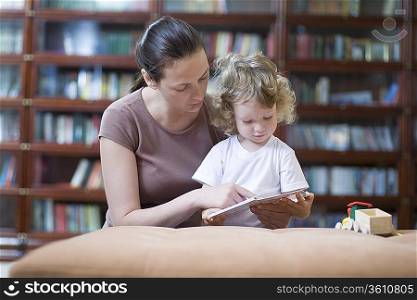 Brunette woman teaches blonde toddler how to read