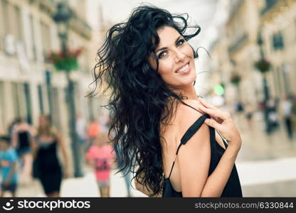 Brunette woman wearing casual clothes in the street. Young girl with curly hairstyle standing in urban background with black shirt.