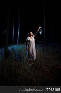 Brunette woman with gas lantern lighting up forest at night