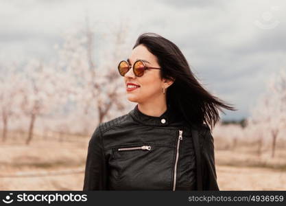 Brunette woman with leather jacket surrounded of flowery almond trees