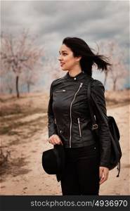 Brunette woman with leather jacket walking on a path with flowered almond trees