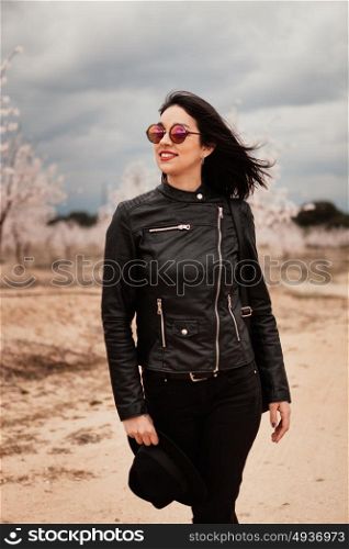 Brunette woman with leather jacket walking on a path with flowered almond trees