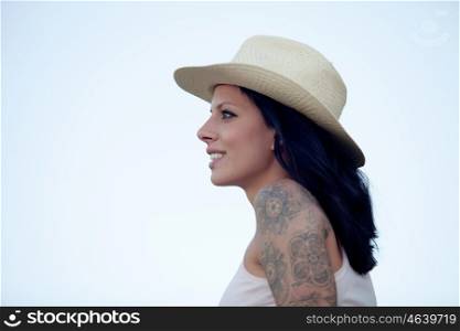 Brunette woman with straw hat and tattoo on the arm looking forward