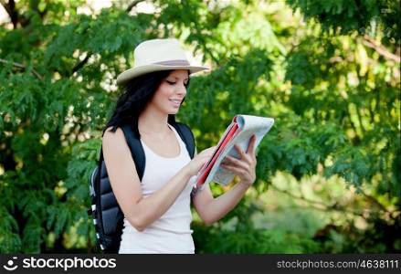 Brunette woman with straw hat walking through the woods while referring to a map