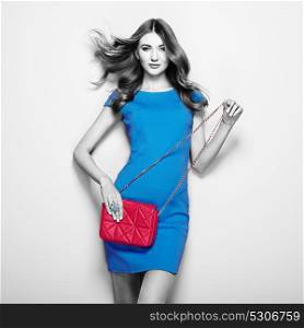 Brunette Young Woman in Elegant Blue Dress. Girl Posing on a White Background. Jewelry and Hairstyle. Girl with Red Handbag. Fashion photo