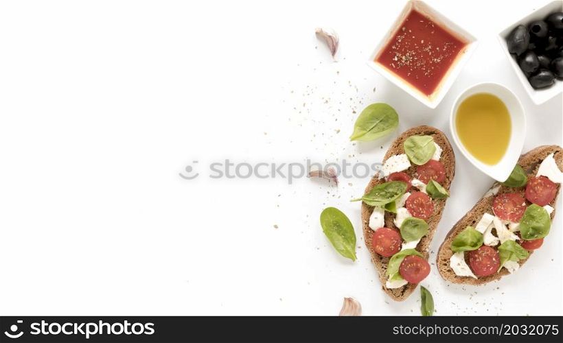 bruschetta with cheese tomato basil leaves topping near sauce olives oil garlic clove white surface
