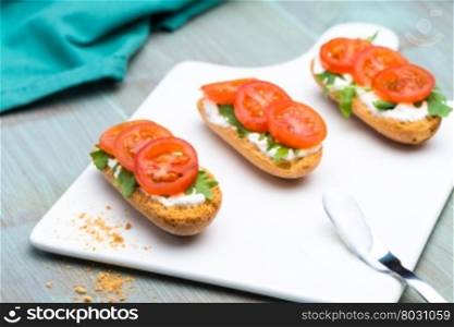 Bruschetta with cottage cheese, tomatoes and arugula served on white creamic tray.