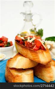 Bruschetta With Olive Oil. Bruschetta on a turquoise plate with toasted baguette slices and more tomato, basil, garlic and olive oil including grated asiago cheese in a small white containers