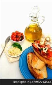 Bruschetta With Olive Oil. Bruschetta on a turquoise plate with toasted baguette slices and more tomato, basil, garlic and olive oil including grated asiago cheese in a small white containers