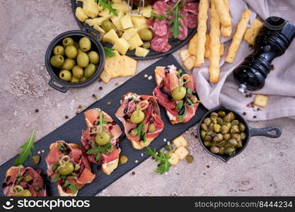 bruschetta with prosciutto ham and capers with traditional antipasto meat plate on background.. bruschetta with prosciutto ham and capers with traditional antipasto meat plate on background