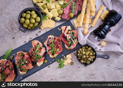 bruschetta with prosciutto ham and capers with traditional antipasto meat plate on background.. bruschetta with prosciutto ham and capers with traditional antipasto meat plate on background