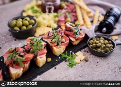 bruschetta with prosciutto ham and capers with traditional antipasto meat plate on background.. bruschetta with prosciutto ham and capers with traditional antipasto meat plate on background