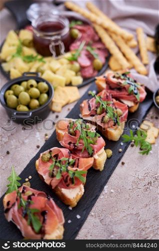 bruschetta with prosciutto ham and capers with traditional antipasto meat plate on background.. bruschetta with prosciutto ham and capers with traditional antipasto meat plate on background
