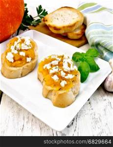 Bruschetta with pumpkin, salted feta cheese in a plate, garlic, basil and parsley, towel and vegetable on a wooden board background