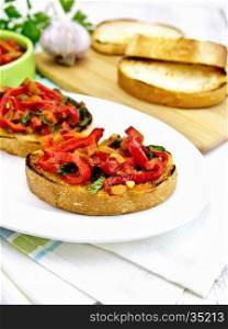 Bruschetta with roasted tomatoes, peppers, garlic, onions and parsley in a plate on a kitchen towel on the background of wooden boards