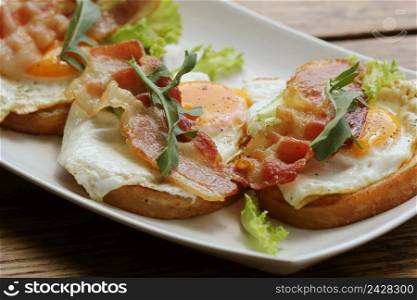 Bruschetta with rucola, chrispy bacon and poached egg served on white plate.. Bruschetta with rucola, chrispy bacon and poached egg served on white plate