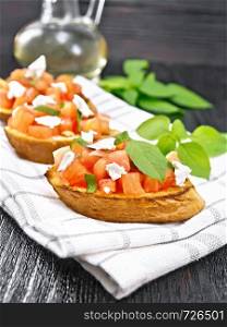 Bruschetta with tomato, basil and soft cheese on a napkin on wooden board