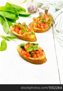 Bruschetta with tomato, basil and spinach, fresh spinach leaves, napkin, garlic and vegetable oil in decanter on wooden board background