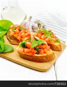 Bruschetta with tomato, basil and spinach on a plate, fresh spinach leaves, napkin and vegetable oil in a decanter against white wooden board