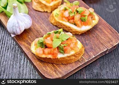Bruschetta with tomato, basil and spinach on a plate, garlic and fresh green leaves on a wooden board background