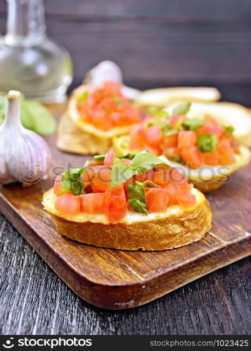 Bruschetta with tomato, basil and spinach on a plate, vegetable oil in a decanter against a dark wooden board