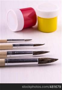 brush set for artist and jars with a paint on white wooden background