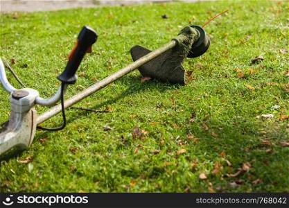Brushcutter mower lying on green grass. Seasonal garden cleaning moder objects concept.. Mower brushcutter on green grass