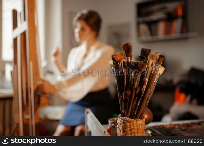 Brushes collection, female artist works at the easel in studio on background. Creative paint, painter drawing portrait in workshop