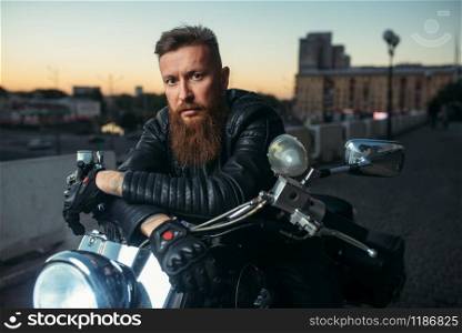 Brutal bearded biker poses on chopper in city, front view. Vintage bike, rider on motorcycle. Brutal bearded biker poses on chopper, front view